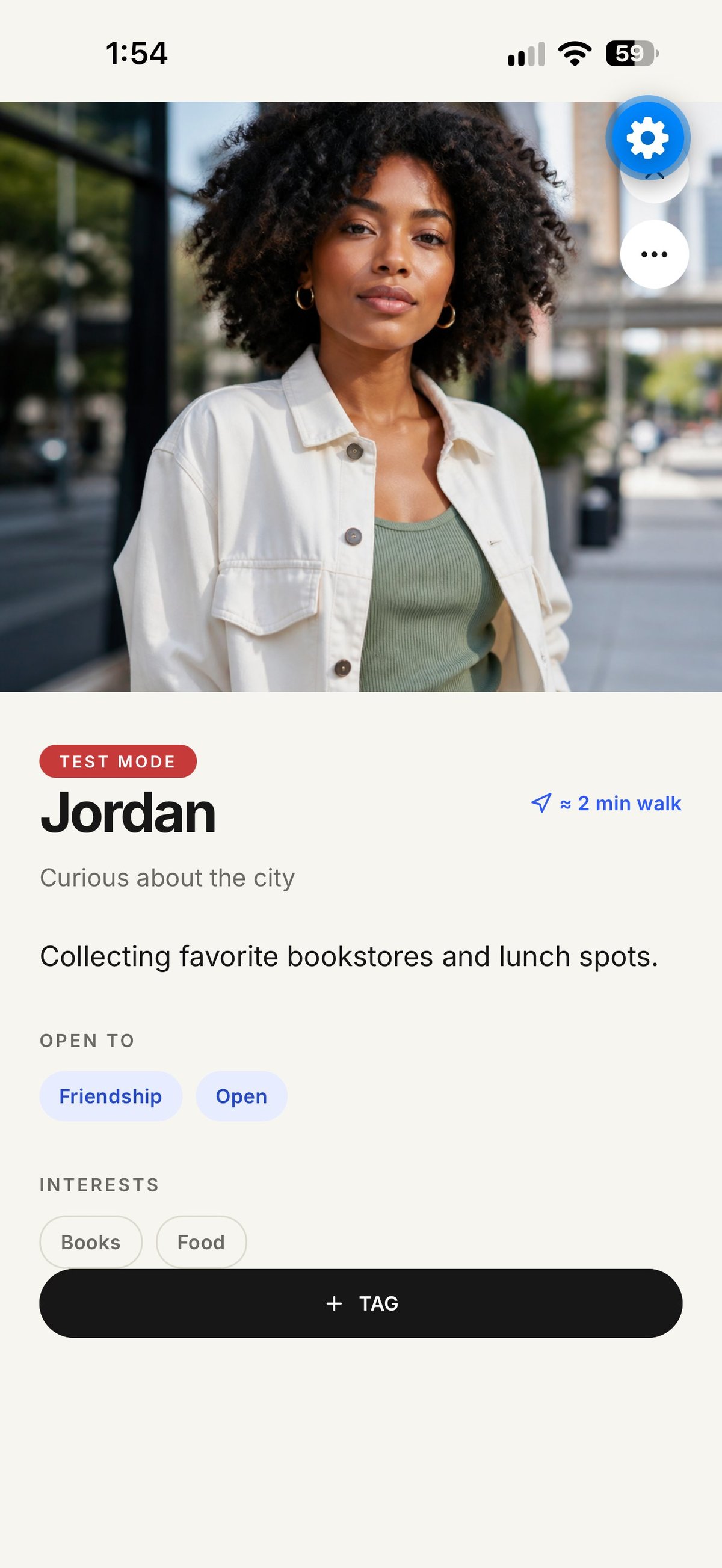 Profile photo of Jordan, a woman with curly black hair wearing a white jacket over a green top, smiling at camera on urban street background